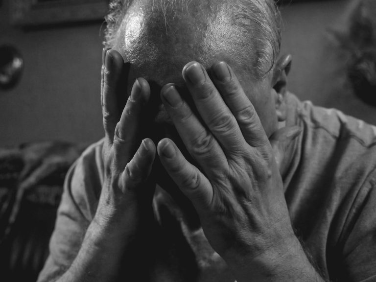 a grayscale photo of an elderly man covering his face