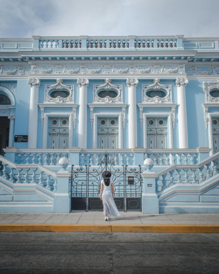woman in white dress standing in front of culture centre in merida mexico